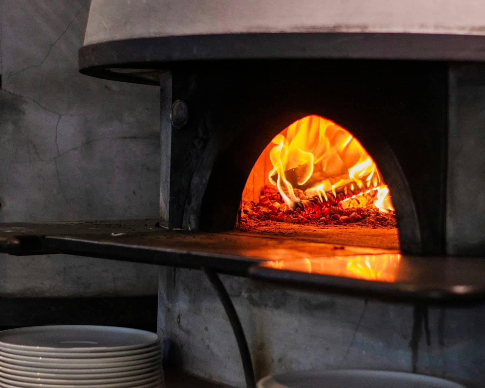 Holzofen mit Flammen, in dem eine Pizza gebacken wird